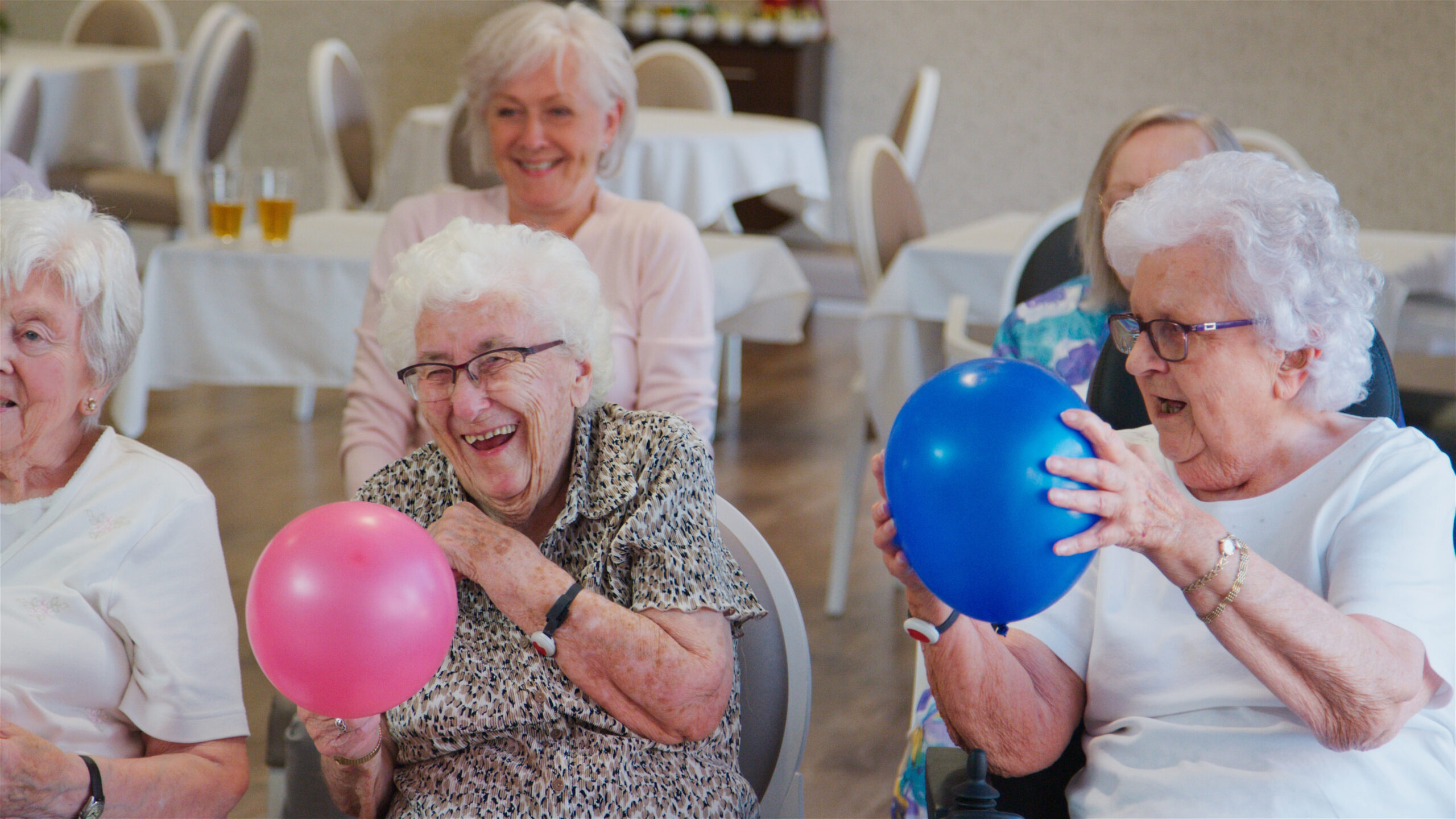Carer,Leading,Group,Of,Seniors,In,Activity,With,Balloons,In